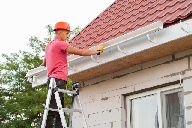 Gutter Installation in Salem roof by employee with safety hat on